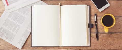 Open notebook with cup of coffee,newspaper,smartphone on wooden desk.